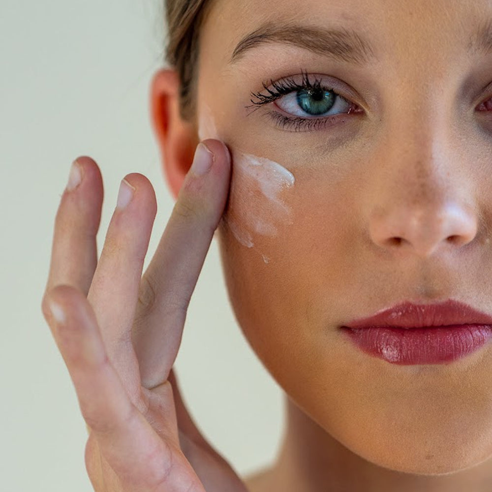 Woman applying cream to her face with a neutral background