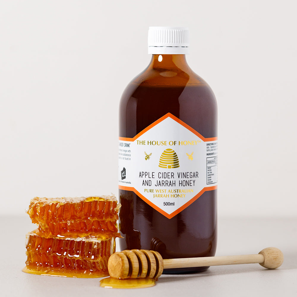 Bottle of apple cider vinegar and jarrah honey with honeycomb and dipper on a light background