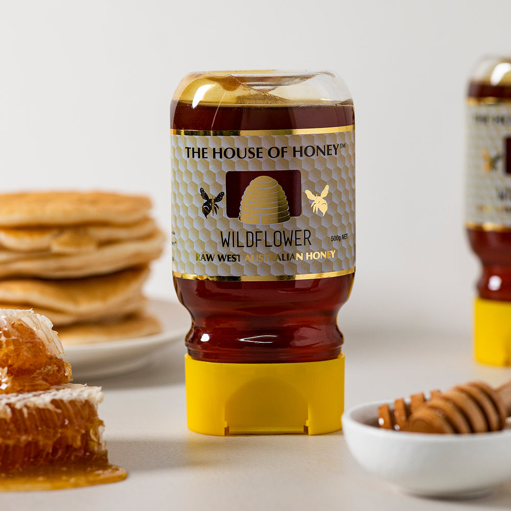 Bottle of The House of Honey wildflower honey with pancakes and honeycomb in the background