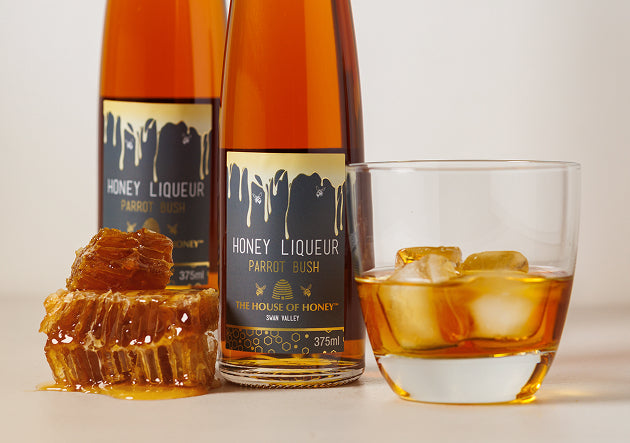 Two bottles of Honey Liqueur Parrot Bush with a glass of the liqueur and honeycomb on a light background.