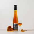 Bottle of honey liqueur with a glass of honey liqueur and honeycomb on a white background