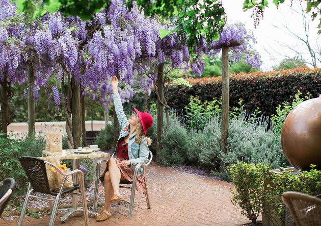 Woman in a garden with wisteria, sitting under a tree with purple flowers.